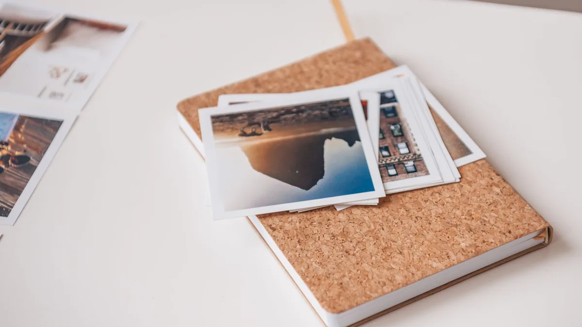 A stack of printed photographs spread out beside an open notebook