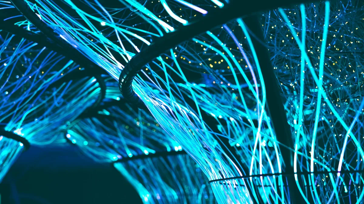 Glowing blue optical fibres fanning out in the dark, suggesting machine processing