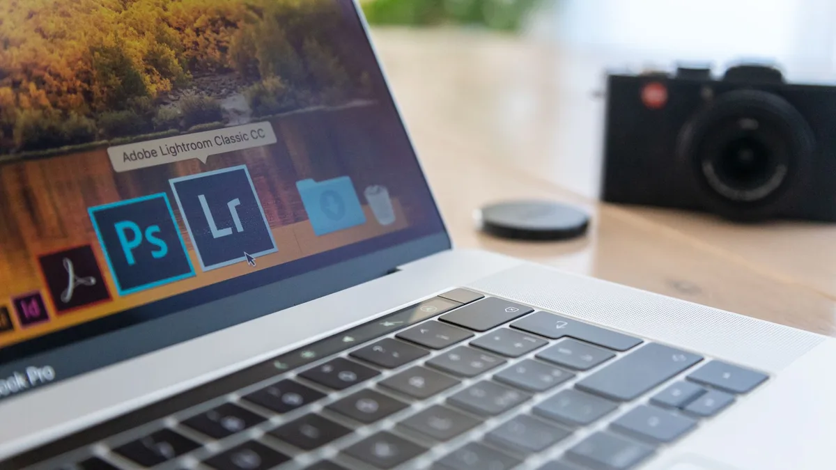 Laptop screen showing photo editing software icons, with a film camera on the desk beside it